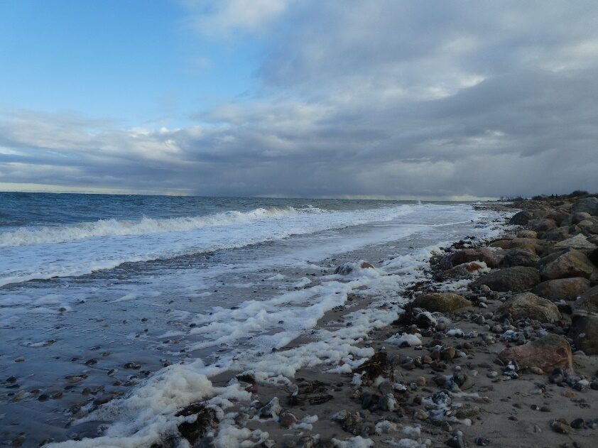 Strandabschnitt in Hohenfelde nach der Sturmflut Oktober 2023 mit Wellen, Wolken und angeschwemmten Gesteinen