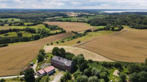 Drohnenbild, im Vordergrund das Eiszeitmuseum, dahinter die Kulturlandschaft mit Feldern, Wiesen, Wäldern und Knicks, im Hintergrund der Selenter See